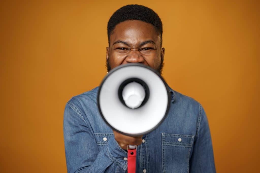 Young african american guy making annoucement with megaphone against yellow background